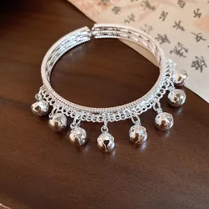 Close-up of an ethnic style silver bangle featuring bell charms and a textured open band