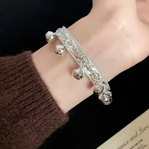 Close-up detail showing the metallic texture and dangling bells of the silver bangle