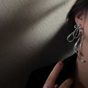 Close-up of an oversized silver metallic bow earring featuring a sparkling diamond accent.