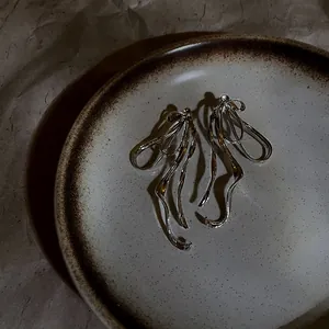 Macro view of silver bow-shaped earrings with long tassel drapes on a ceramic plate