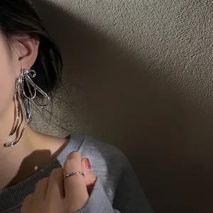 Close-up of a stylish silver bow earring with fluid metallic design on model's ear.