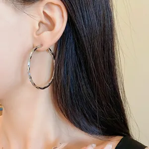 Primo piano di orecchini a cerchio geometrici in argento con trama intrecciata su modella.