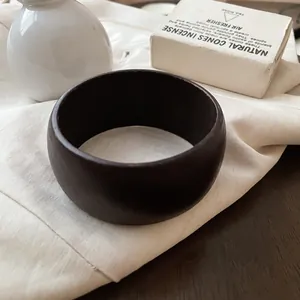 Primer plano de un brazalete redondo minimalista de acrílico oscuro en tela blanca.