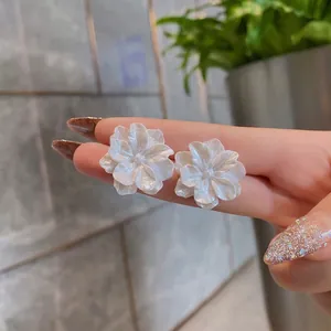 Close-up of elegant white acrylic flower stud earrings with a pearlescent finish on a hand