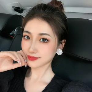 Elegant white acrylic flower stud earrings worn by a model in a stylish car setting.
