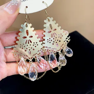 Detail showing ornate gold-tone fan earrings with crystal teardrops and delicate metal chains.