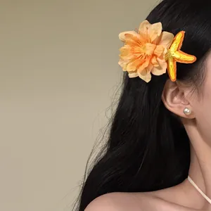 Detailed view of orange fabric flower and yellow starfish hair clip on long dark hair