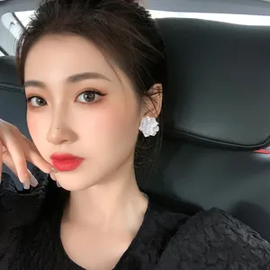 Close-up view of elegant white acrylic flower stud earrings worn by a female model in a car