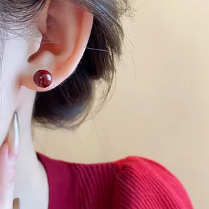 Primer plano detallado de un elegante pendiente de bola rojo cereza usado en la oreja del modelo