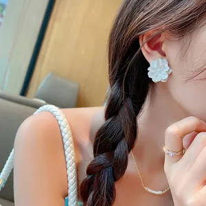 Close-up detail of a delicate white acrylic flower stud earring worn by a model