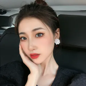 Elegant white acrylic flower stud earrings worn by a model inside a car setting