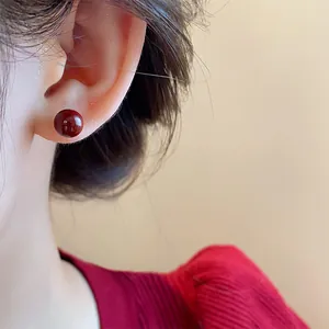 Primer plano de los pendientes de bola rojos Ankora vintage en la oreja de una modelo.