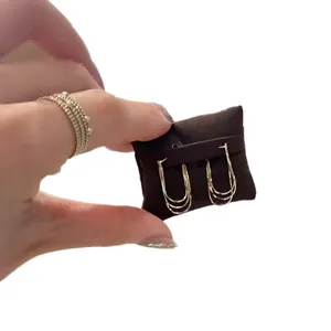 Elegant minimalist multi-layered gold hoop earrings displayed on a dark brown cushion