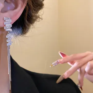 Dettaglio di orecchini con nappe argentate e pietre di zircone su modella asiatica.