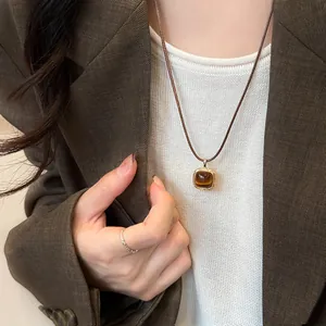 Close-up of vintage rounded-square pendant with tiger eye stone and brown leather cord