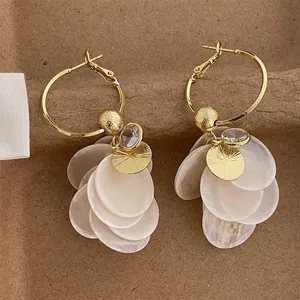 Close-up of zircon and white shell tassel earrings with gold hoops for beach style