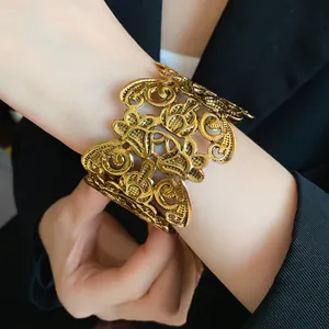 Detail van een vintage gouden manchetarmband met opengewerkt bloemmotief en metaalglans