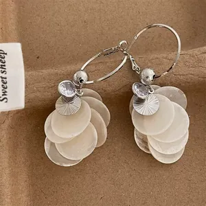 Detailed view of silver hoop earrings featuring white shell dangles and zircons.