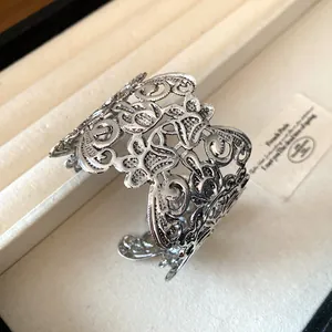 Detailweergave van een vintage zilveren metalen manchetarmband met opengewerkt bloemmotief.