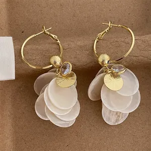 Macro detail of elegant gold hoop earrings with white shell petals and sparkling zircon