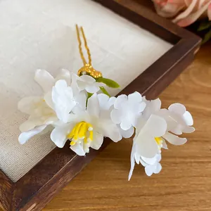 Elegant white fabric flower hairpin with yellow stamen detail on a wooden frame background