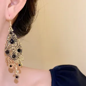 Close-up of vintage gold teardrop earrings featuring black rhinestones and floral tassels