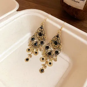 Close-up of vintage gold water-drop earrings with black rhinestones and tassels.