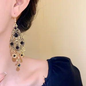 Close-up of vintage gold drop earrings featuring black rhinestones and floral tassels