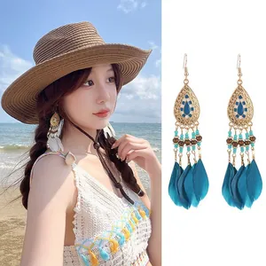 Bohemian teal feather tassel earrings with gold-tone drop design on beach background