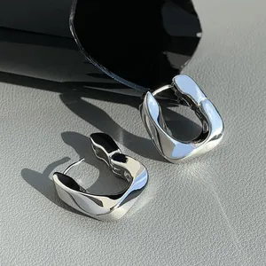 Macro view of polished silver geometric U-shaped hoop earrings on grey textured leather