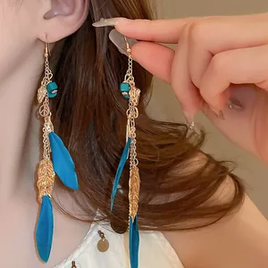 Detailed view of bohemian dangle earrings with blue feathers and gold leaf tassels.