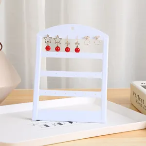 Vista detallada de un soporte para pendientes blanco minimalista con elegantes pendientes rojos y oro