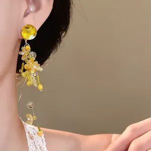 Primo piano di orecchini pendenti con nappa a fiore giallo indossati da una modella elegante.