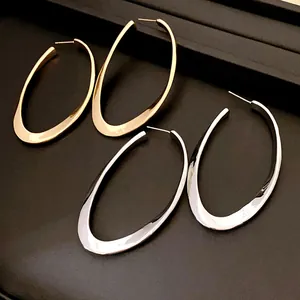 Detailed macro view of minimalist gold and silver oval hoop earrings on black tray.