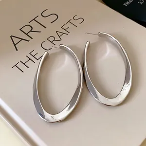 Close-up of silver-finish geometric oval hoop earrings with polished mirror surface