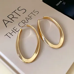 Detailed view of elegant gold-toned oval twisted hoop earrings resting on a book surface