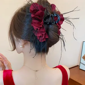 Eleganter weinroter Rosen-Haarclip aus Stoff mit schwarzen Federn am gestylten Haar.
