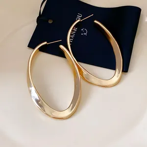 Detailed close-up view of large golden hollow oval earrings with a twisted design
