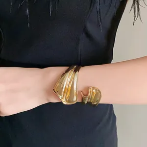 Detail view of a bold gold irregular distorted open cuff bracelet on a female wrist