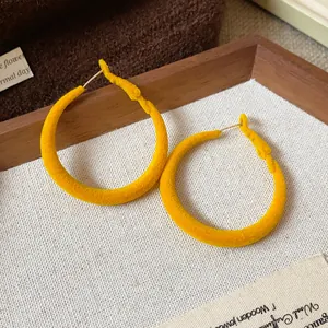 Dettaglio di orecchini a cerchio floccati giallo vibrante con una morbida consistenza vellutata