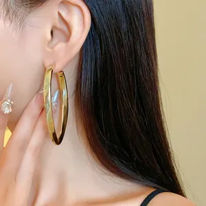 Detail view of stylish gold-finished oval hollow hoop earrings on a model's ear.