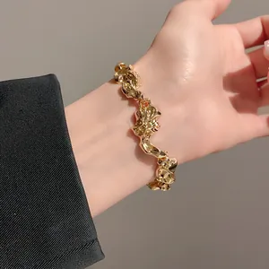 Detalle de una pulsera de metal dorado retorcido e irregular en la muñeca modelo