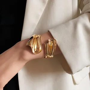 Close-up of a gold irregular open cuff bracelet worn with a white blazer