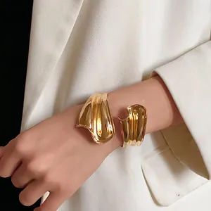 Detailed view of an irregular gold-colored open metal cuff bracelet on a female wrist.
