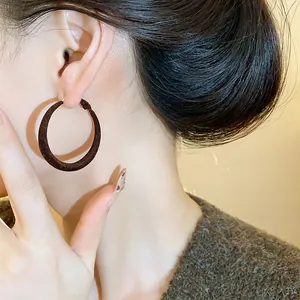 Primo piano di un orecchino a cerchio floccato scuro minimalista sull'orecchio di donna.