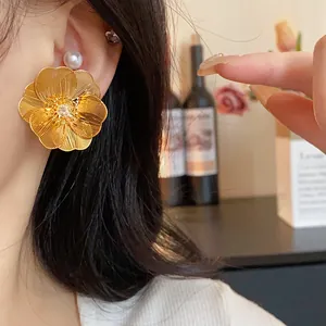 Dettaglio di un grande orecchino a fiore dorato con centro in zircone su una modella