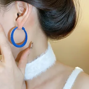 Primo piano di un orecchino a cerchio floccato blu indossato sull'orecchio