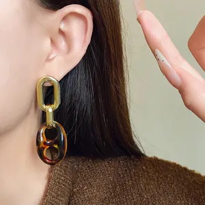 Detailed view of elegant vintage tortoiseshell chain earrings on model with brown sweater