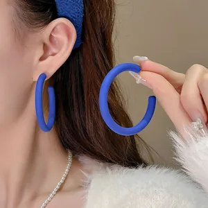 Dettaglio ravvicinato di orecchini a cerchio blu opaco a forma di C indossati da una modella
