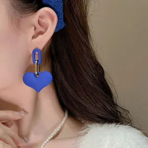 Primo piano di eleganti orecchini pendenti a cuore blu Klein indossati da una modella.